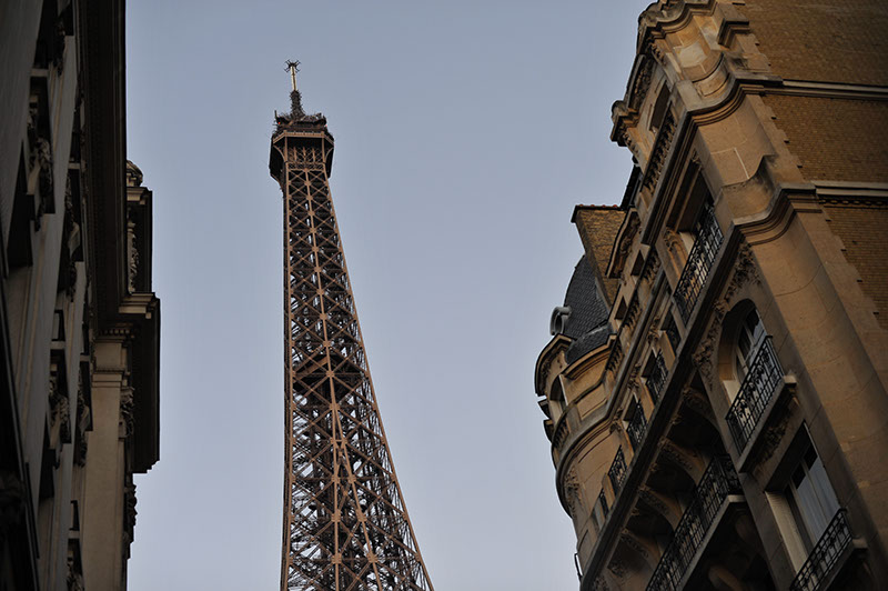 looking up at he Eiffel tower, through buildings